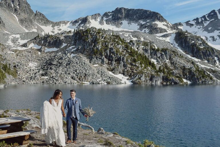 An elopement couple walk along the water's edge of Marriage Lake in Pemberton, BC