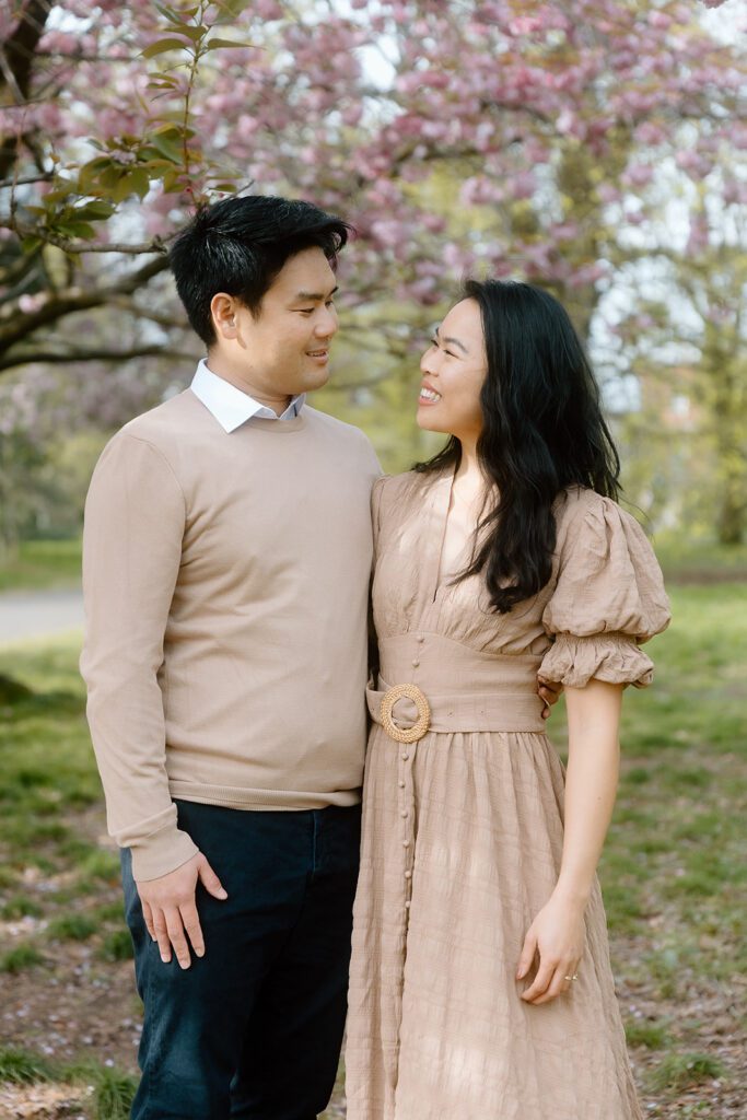 A man and woman look at each other smiling with blossom tree in the background.