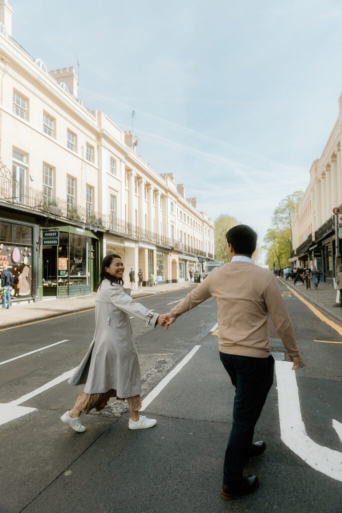 A man and woman cross the street near Greenwich market in London, hand in hand.