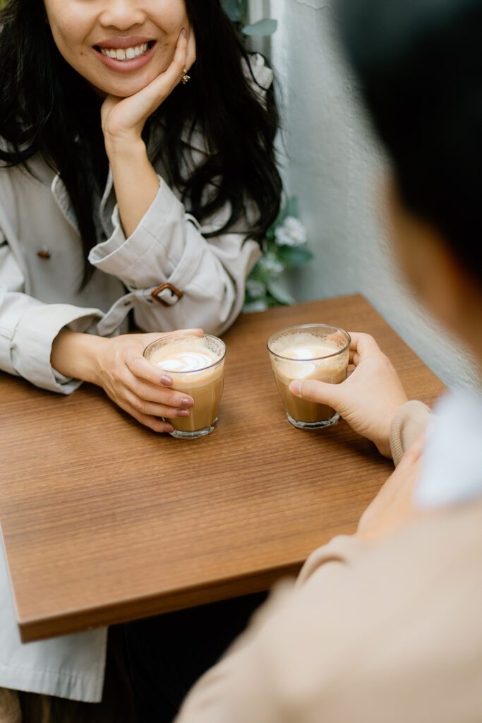 Two lattes on a coffee shop table held by a man and woman.